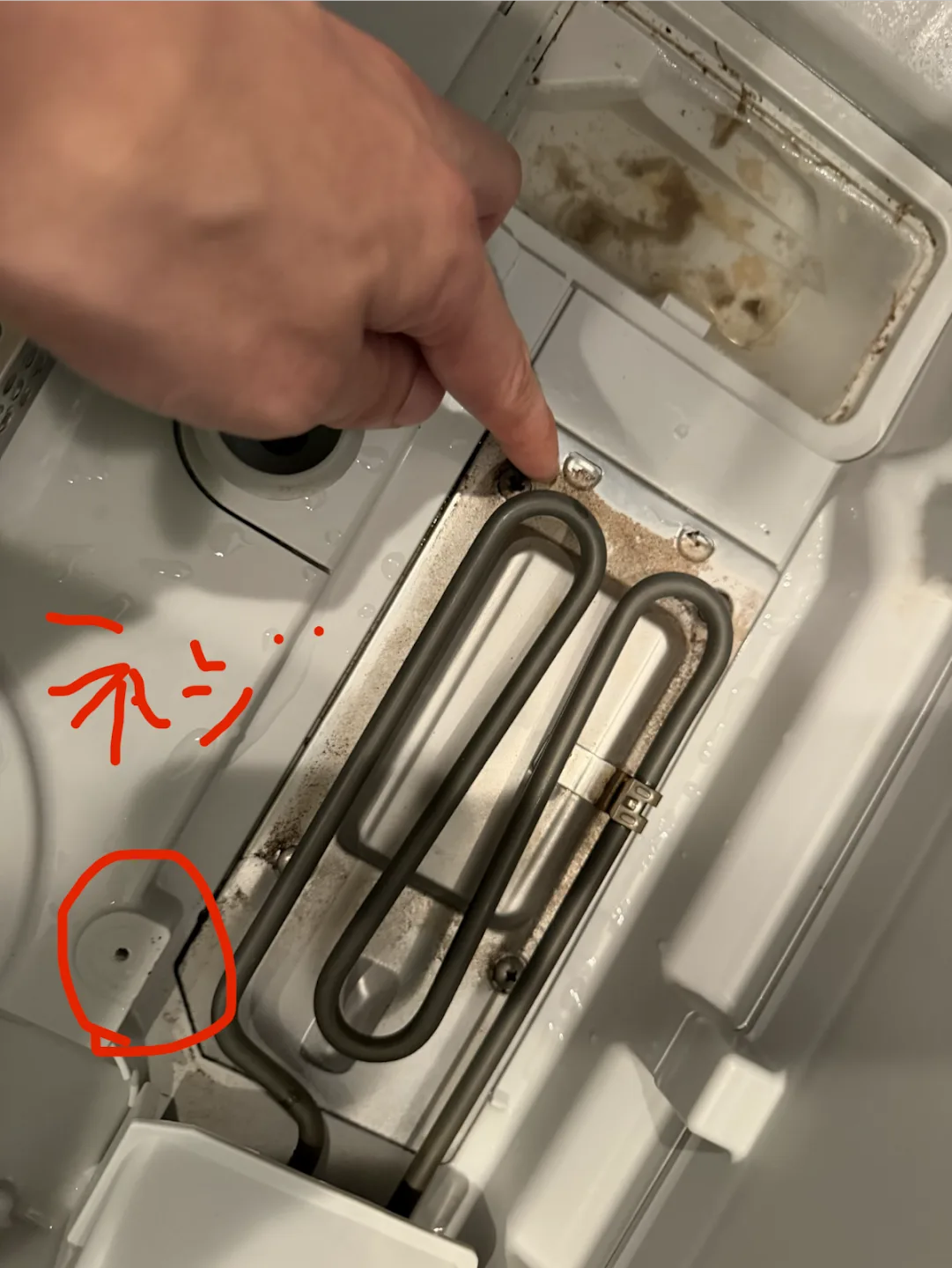 アルミカバーを外した食洗機庫内のヒーター部分。指が1本目のネジを指しており、もう1本のネジが赤丸で囲まれている